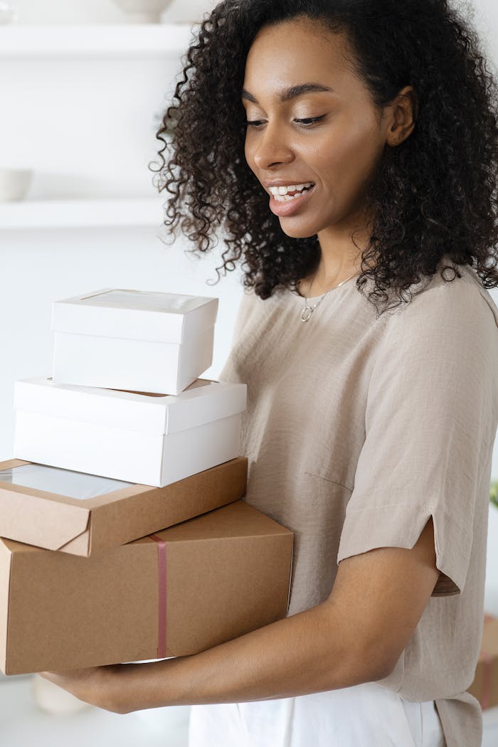 Services A cheerful woman holding multiple cardboard and white packages indoors, expressing happiness.